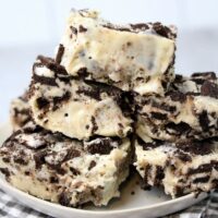 Oreo White Chocolate Fudge stacked on a white plate with gray plaid napkin on a faux concrete back drop.