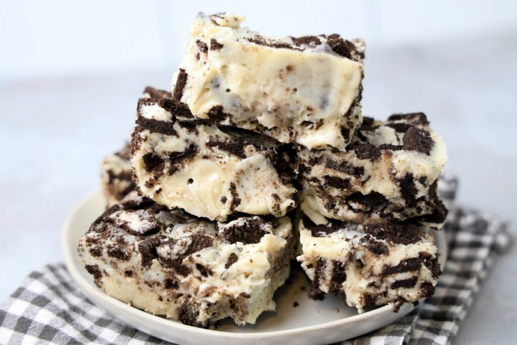 Oreo White Chocolate Fudge stacked on a white plate with gray plaid napkin on a faux concrete back drop.