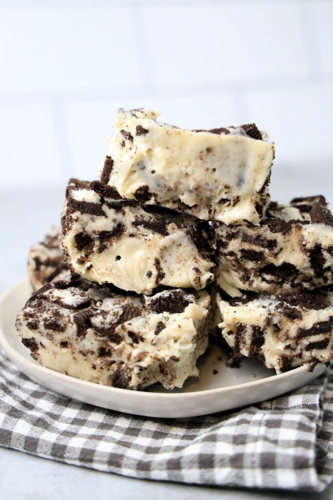 Oreo White Chocolate Fudge stacked on a white plate with gray plaid napkin on a faux concrete back drop.