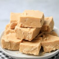 Peanut Butter Fudge stacked on a white plate on a gray plaid napkin with a faux concrete backdrop.