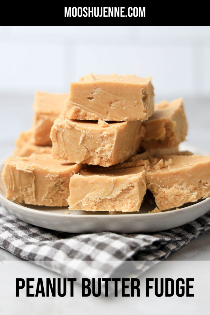 Peanut Butter Fudge stacked on a white plate on a gray plaid napkin with a faux concrete backdrop.