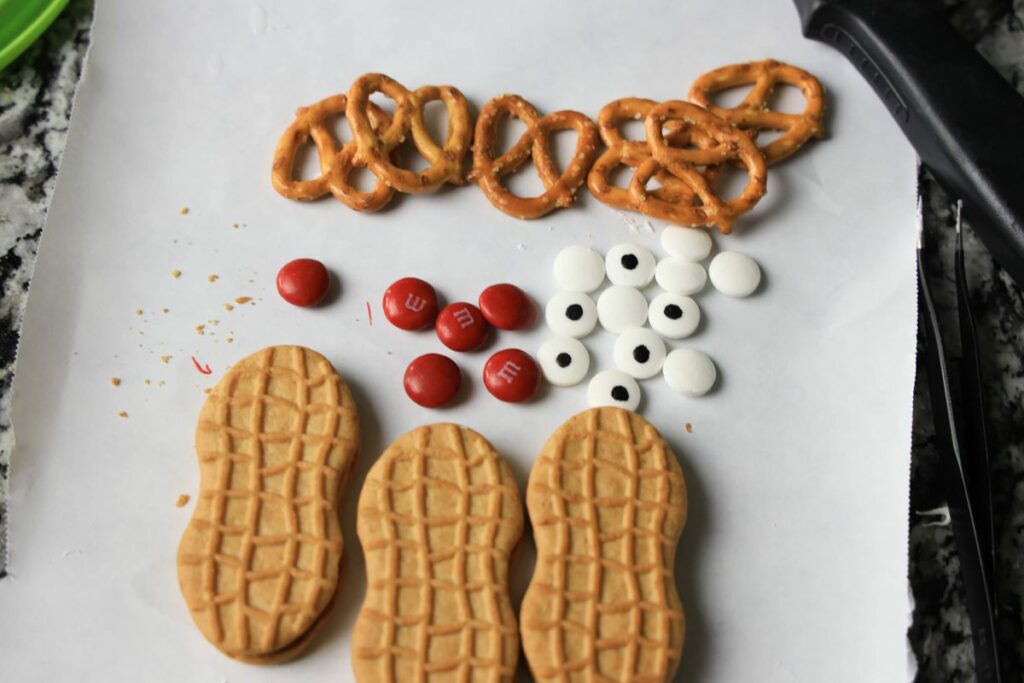 Butter butters, candy eyes, red M&M's, and pretzels on a piece of parchment paper.
