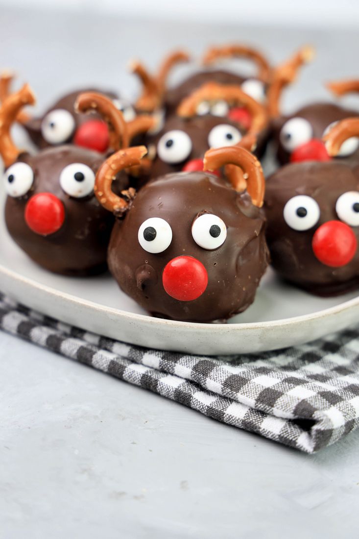 Rudolph orep balls with candy eyes, a red nose, and pretzel antlers on a white plaid with gray plaid napkin and faux concrete backdrop.