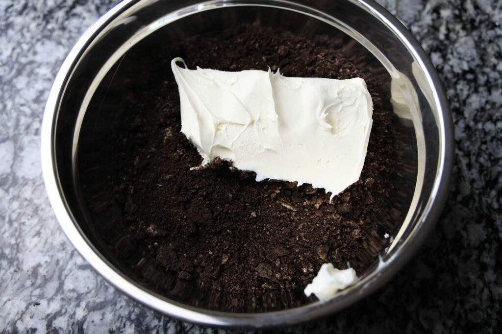 Cream cheese in a bowl with a bunch of Oreo crumbs.