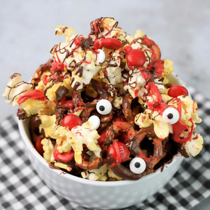 Popcorn with pretzels, red M&M's, chocolate and red drizzle in a white bowl.