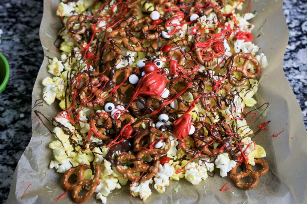 Popcorn, pretzels, and candy eyes with dark chocolate and red candy melts drizzled over them.