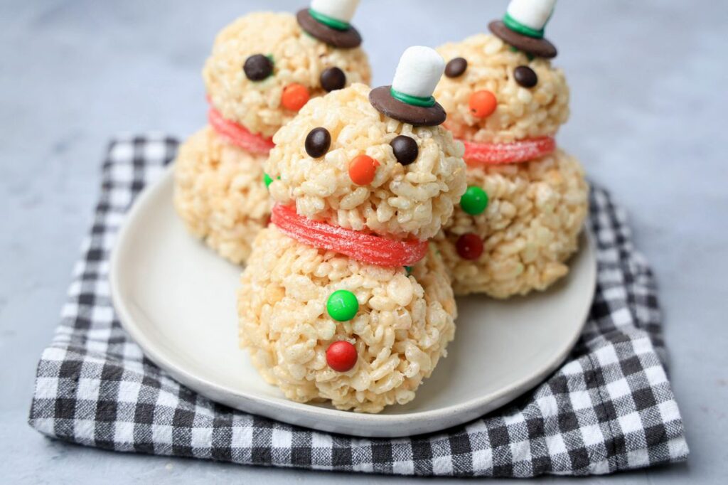 Snowman made from rice krispie treats on a white plate with a plaid napkin.