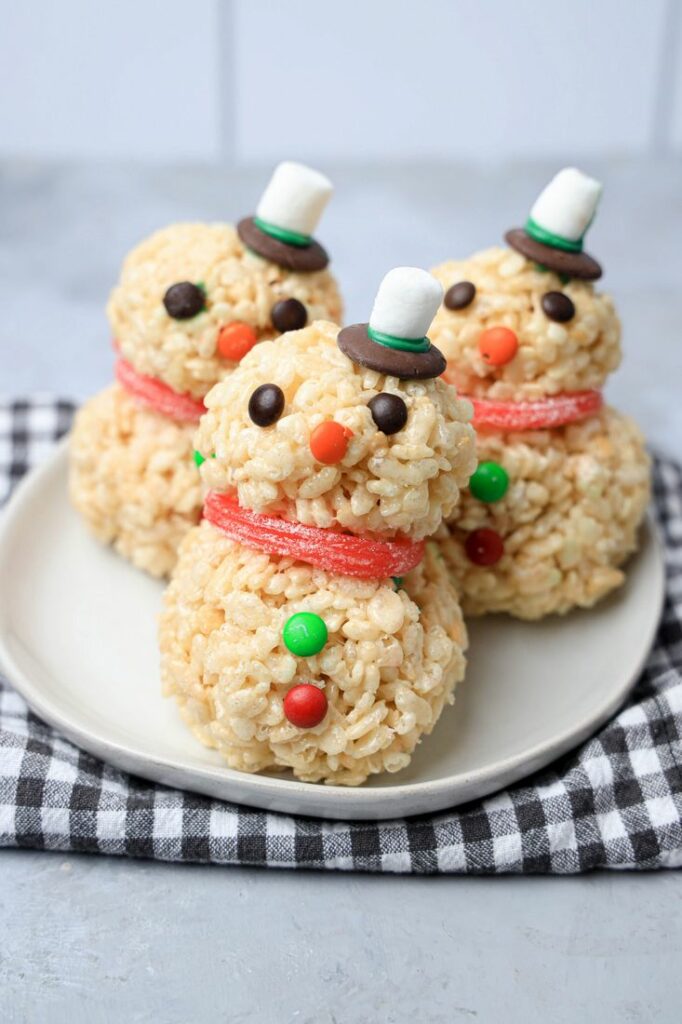 Snowman made from rice krispie treats on a white plate with a plaid napkin.