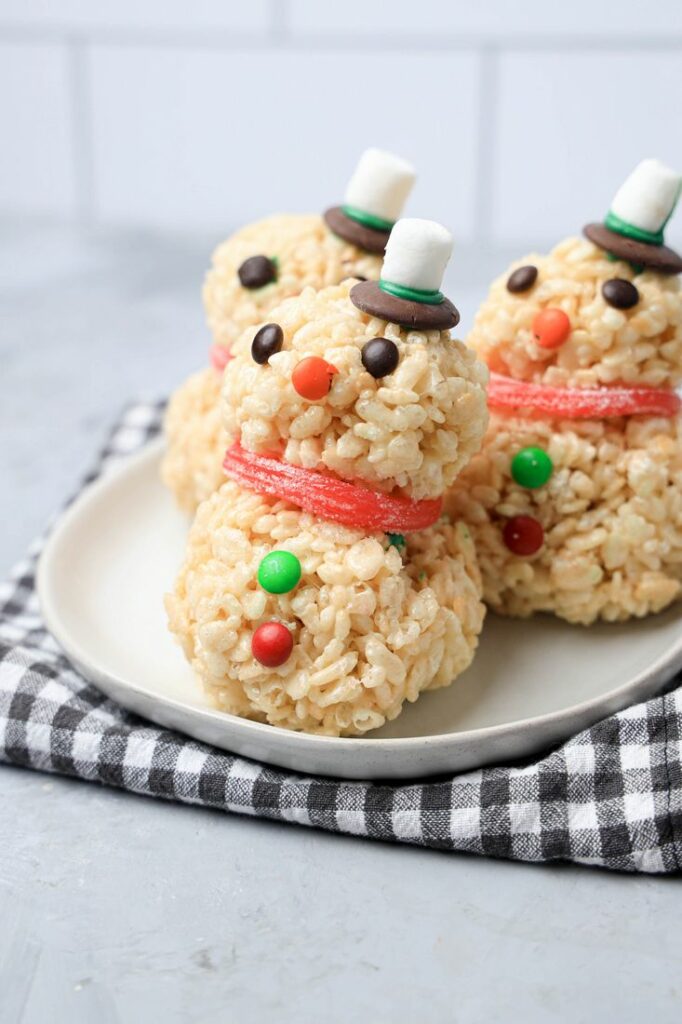 Snowman made from rice krispie treats on a white plate with a plaid napkin.