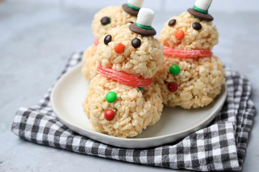 Snowman made from rice krispie treats on a white plate with a plaid napkin.