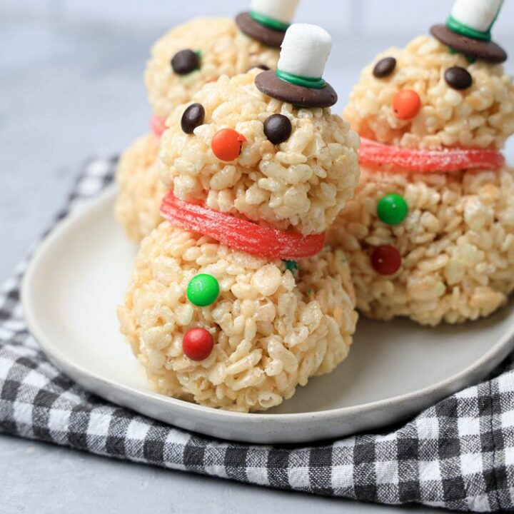 Snowman made from rice krispie treats on a white plate with a plaid napkin.