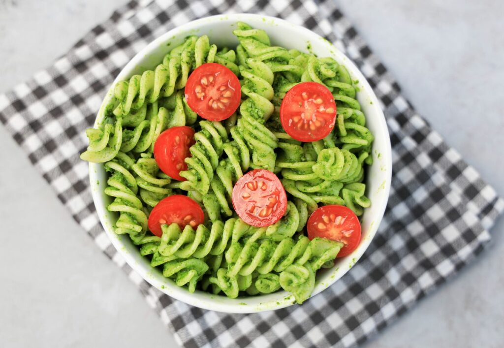 Basil Garlic Spinach Pesto Rotini topped with tomatoes in a white bowl on a gray plaid napkin.