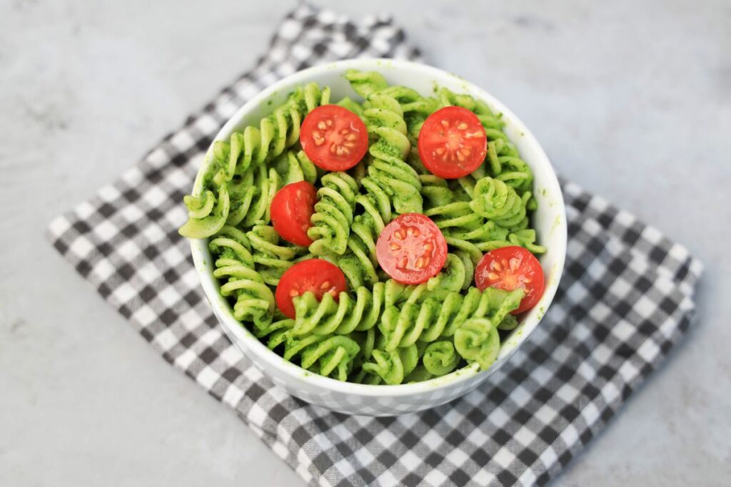 Basil Garlic Spinach Pesto Rotini topped with tomatoes in a white bowl on a gray plaid napkin.