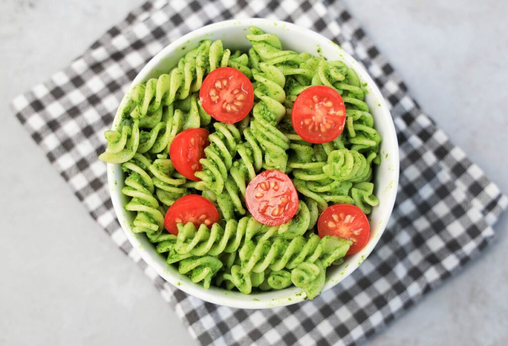 Basil Garlic Spinach Pesto Rotini topped with tomatoes in a white bowl on a gray plaid napkin.