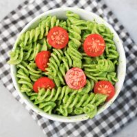 Basil Garlic Spinach Pesto Rotini topped with tomatoes in a white bowl on a gray plaid napkin.