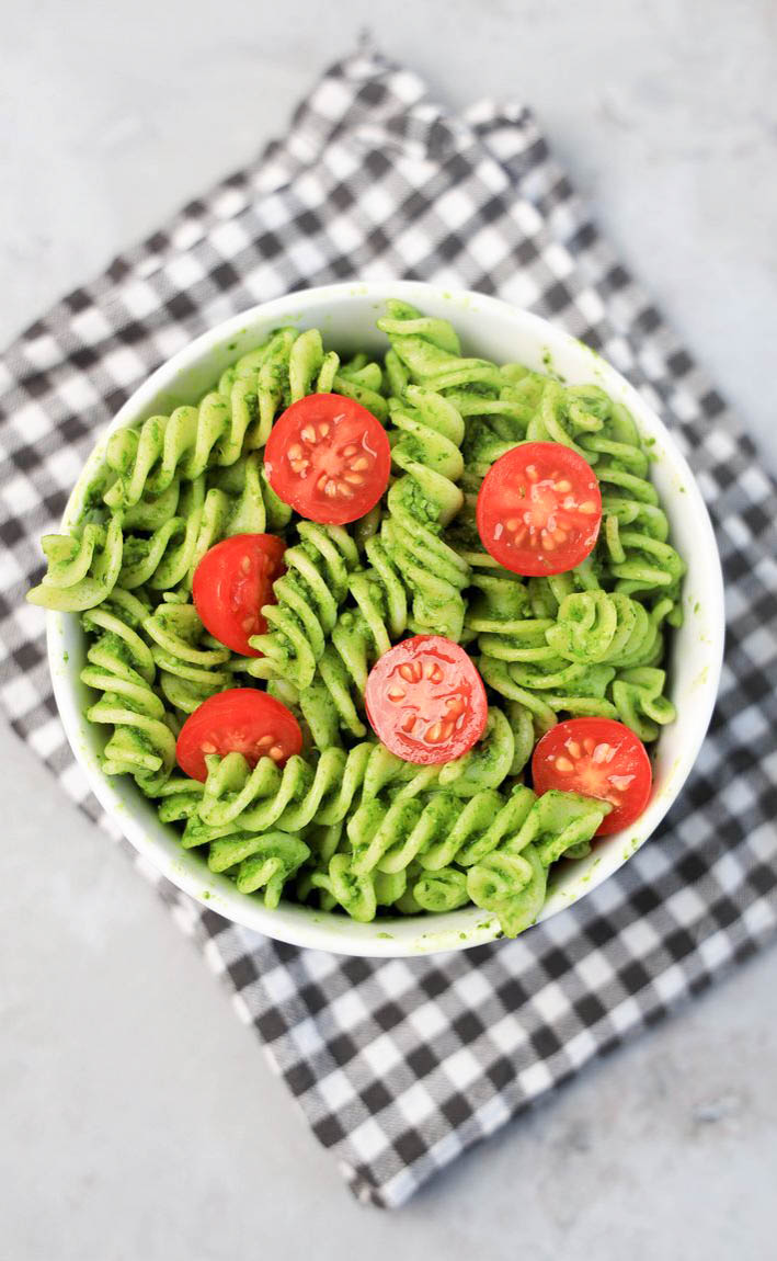Basil Garlic Spinach Pesto Rotini topped with tomatoes in a white bowl on a gray plaid napkin.