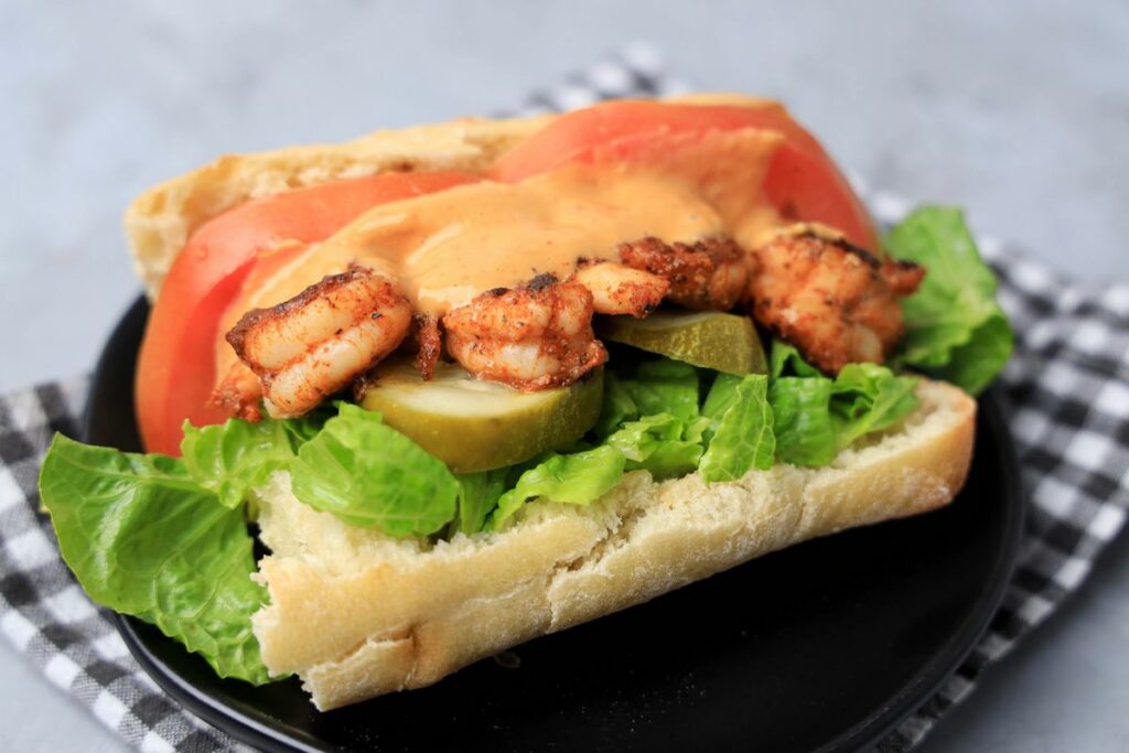 Cajun blackened shrimp po' boy on a black plate with gray plaid napkin on a faux concrete backdrop.