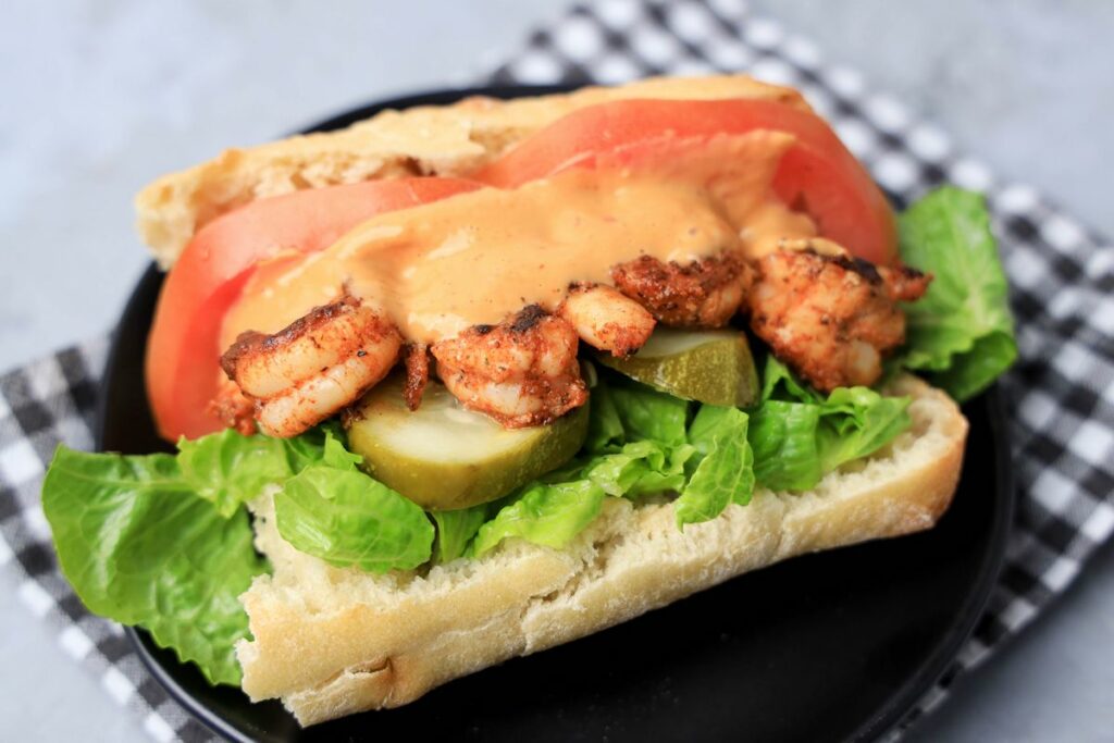 Cajun blackened shrimp po' boy on a black plate with gray plaid napkin on a faux concrete backdrop.