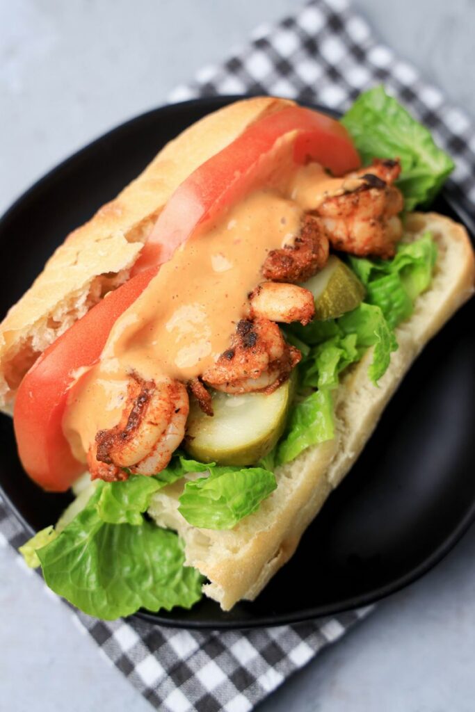 Cajun blackened shrimp po' boy on a black plate with gray plaid napkin on a faux concrete backdrop.