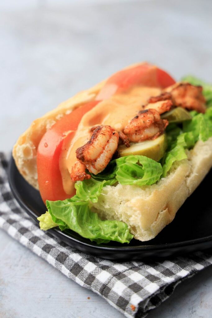 Cajun blackened shrimp po' boy on a black plate with gray plaid napkin on a faux concrete backdrop.