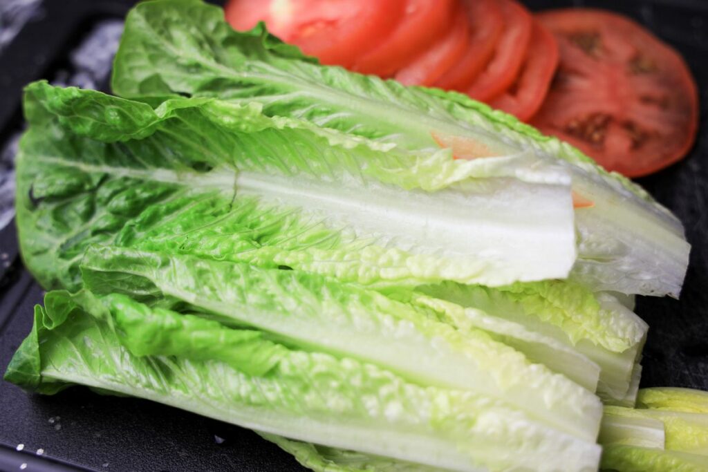 Romaine lettuce and tomato on a black cutting board.