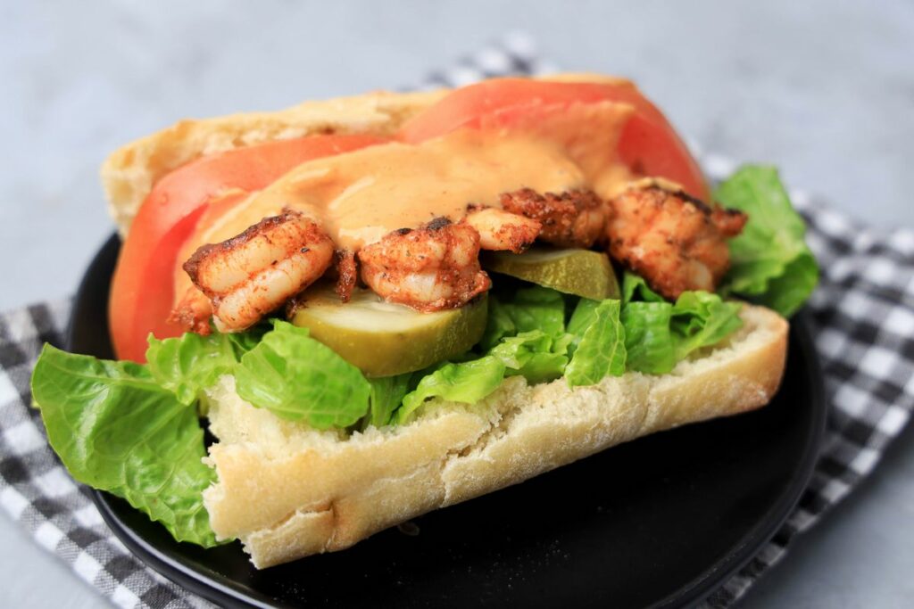 Cajun blackened shrimp po' boys on a black plate with gray plaid napkin on a faux concrete backdrop.