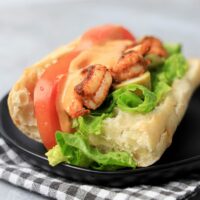 Cajun blackened shrimp po' boys on a black plate with gray plaid napkin on a faux concrete backdrop.