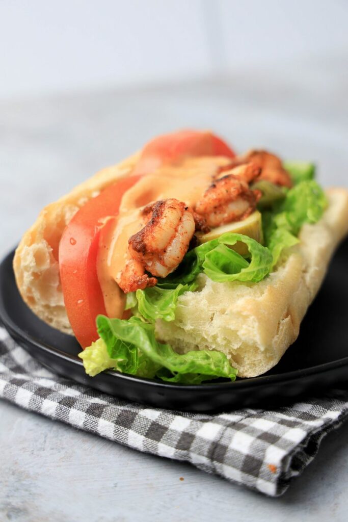 Cajun blackened shrimp po' boys on a black plate with gray plaid napkin on a faux concrete backdrop.