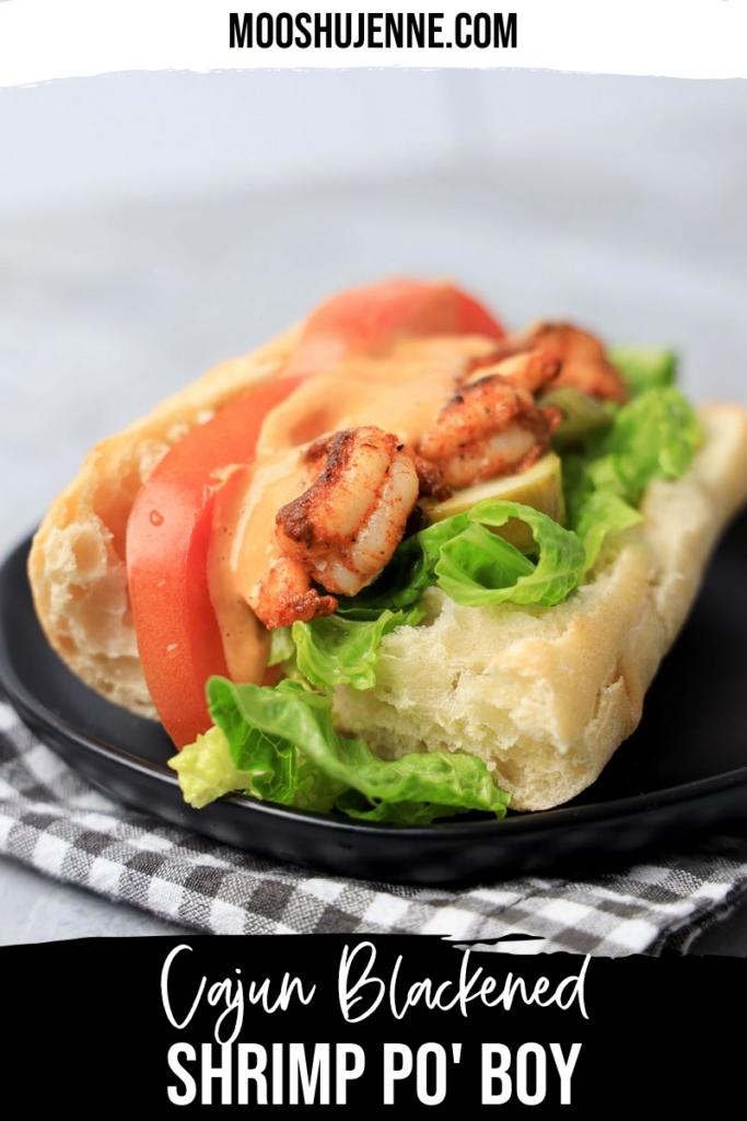 Cajun blackened shrimp po' boy on a black plate with gray plaid napkin on a faux concrete backdrop.