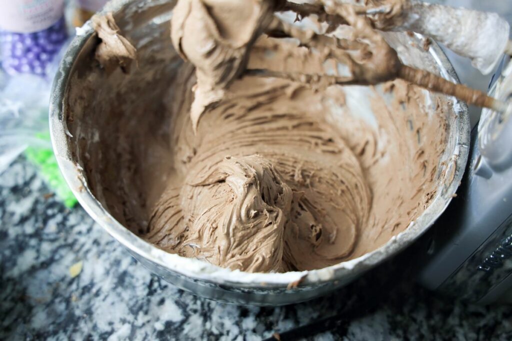 Brownie mixed with cream cheese and cool whip in a bowl with hand mixer.