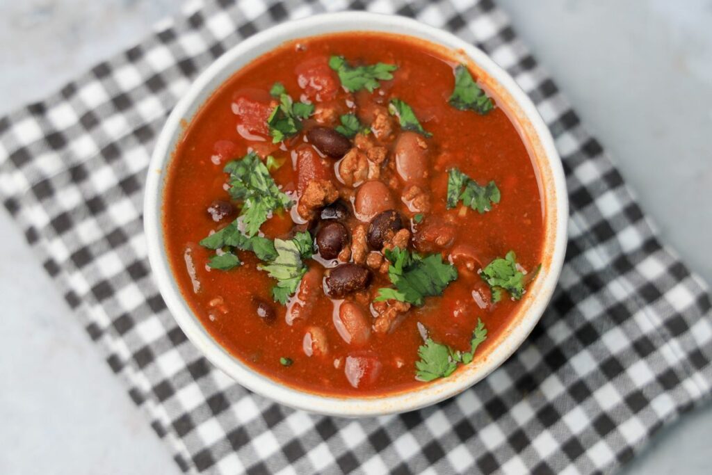 Slow Cooker Beef Chili in a stone bowl with a gray plaid napkin on a faux backdrop.