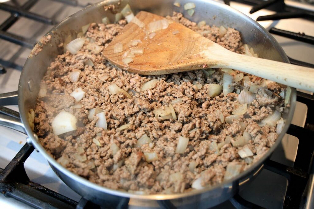 Ground beef in frying pan on a gas stove.