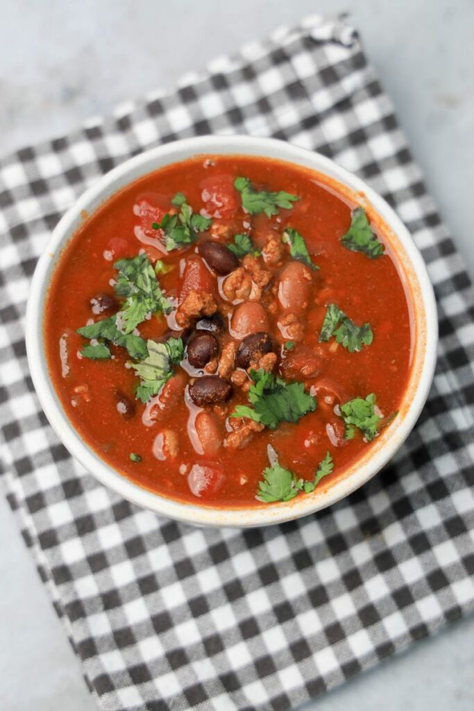 Slow Cooker Beef Chili in a stone bowl with a gray plaid napkin on a faux backdrop.