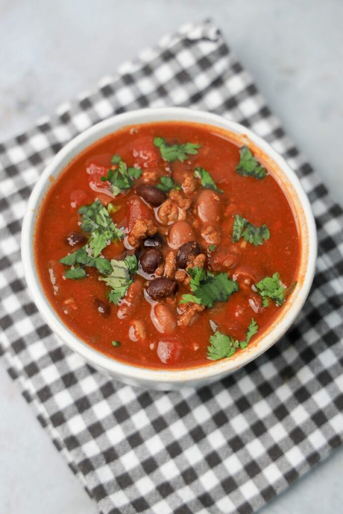 Slow Cooker Beef Chili in a stone bowl with a gray plaid napkin on a faux backdrop.