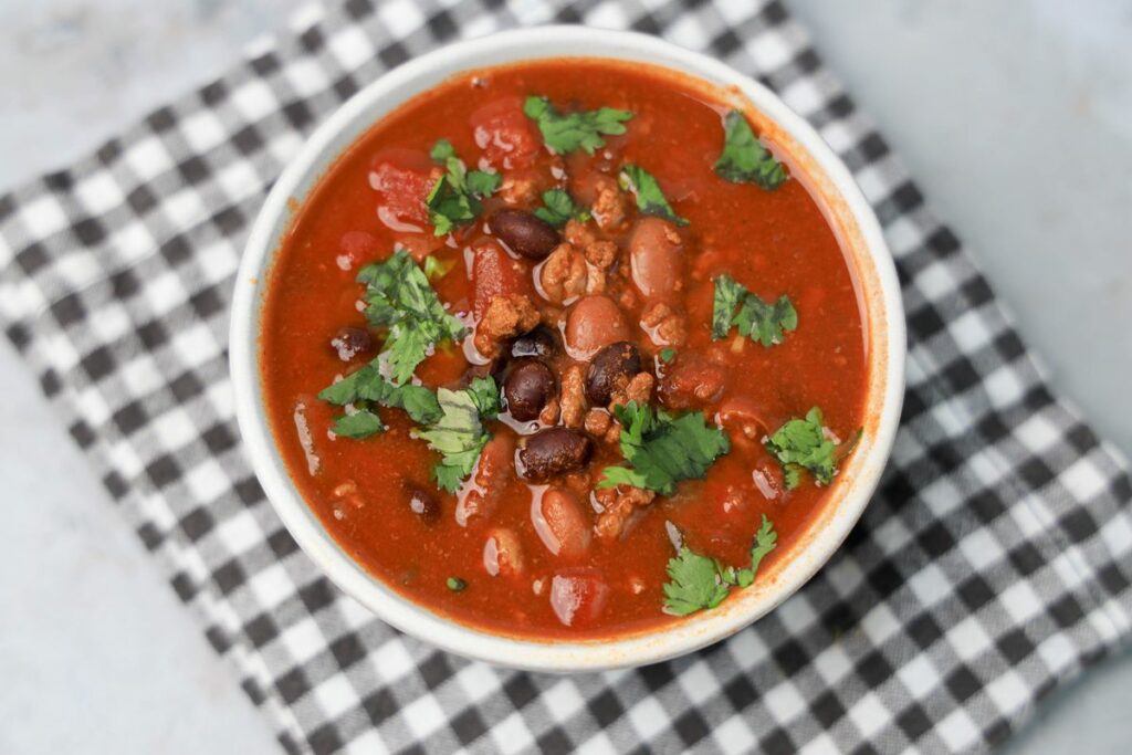 Slow Cooker Beef Chili in a stone bowl with a gray plaid napkin on a faux backdrop.