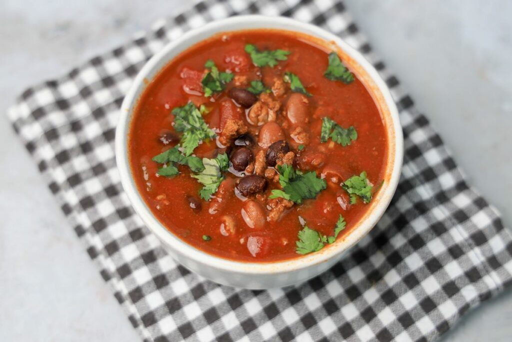 Slow Cooker Beef Chili in a stone bowl with a gray plaid napkin on a faux backdrop.