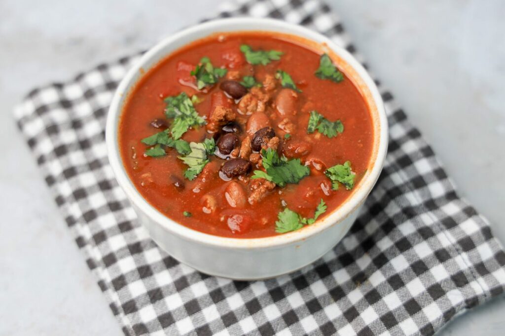 Slow Cooker Beef Chili in a stone bowl with a gray plaid napkin on a faux backdrop.