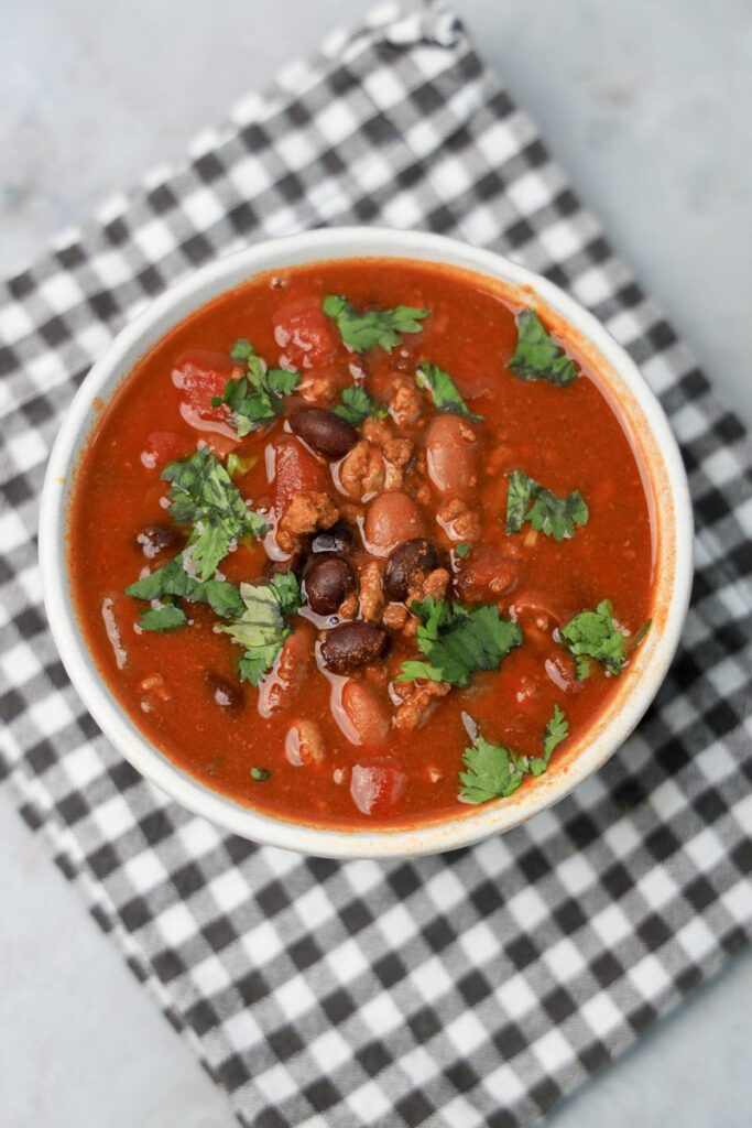 Slow Cooker Beef Chili in a stone bowl with a gray plaid napkin on a faux backdrop.