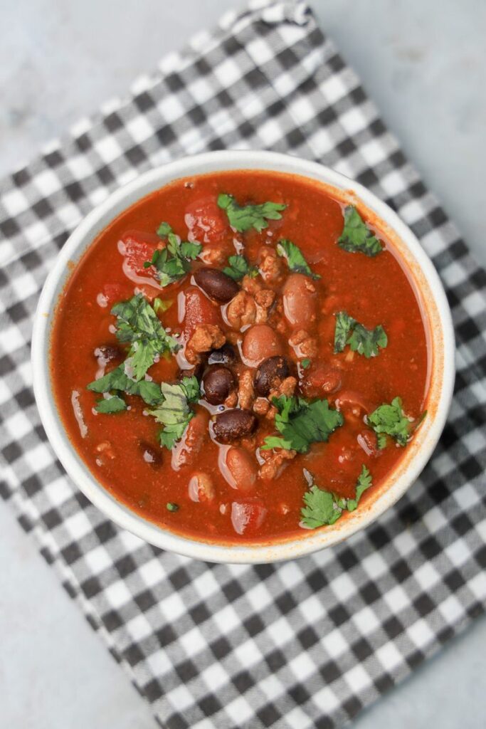 Slow Cooker Beef Chili in a stone bowl with a gray plaid napkin on a faux backdrop.