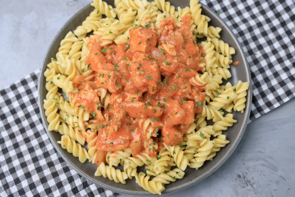 Slow cooker chicken paprikash with rotini noodles on a gray plate with a gray plaid napkin and faux concrete backdrop.