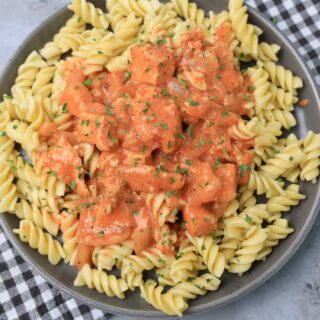 Slow cooker chicken paprikash with rotini noodles on a gray plate with a gray plaid napkin and faux concrete backdrop.