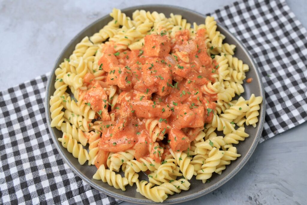 Slow cooker chicken paprikash with rotini noodles on a gray plate with a gray plaid napkin and faux concrete backdrop.