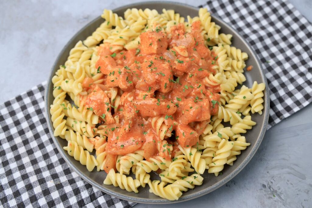 Slow cooker chicken paprikash with rotini noodles on a gray plate with a gray plaid napkin and faux concrete backdrop.