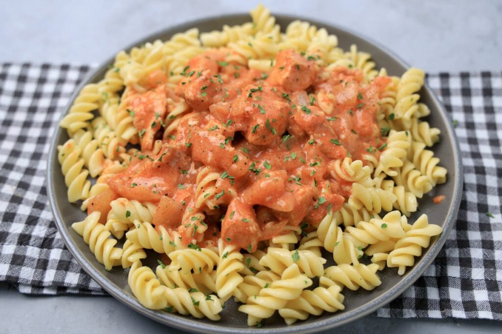 Slow cooker chicken paprikash with rotini noodles on a gray plate with a gray plaid napkin and faux concrete backdrop.