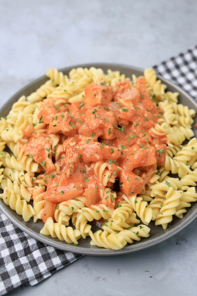 Slow cooker chicken paprikash with rotini noodles on a gray plate with a gray plaid napkin and faux concrete backdrop.