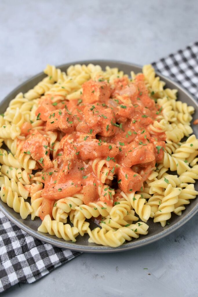 Slow cooker chicken paprikash with rotini noodles on a gray plate with a gray plaid napkin and faux concrete backdrop.