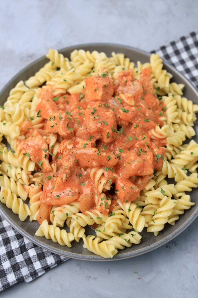 Slow cooker chicken paprikash with rotini noodles on a gray plate with a gray plaid napkin and faux concrete backdrop.