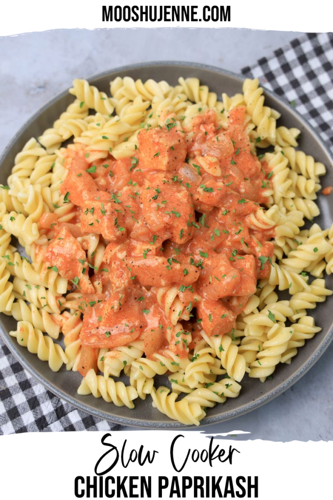 Slow cooker chicken paprikash with rotini noodles on a gray plate with a gray plaid napkin and faux concrete backdrop.