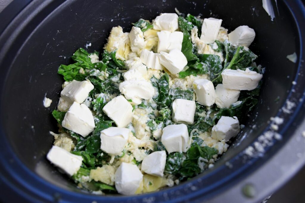 Spinach, mozzarella cheese, parmesan cheese, and garlic in the slow cooker wit chunks of cream cheese on top.