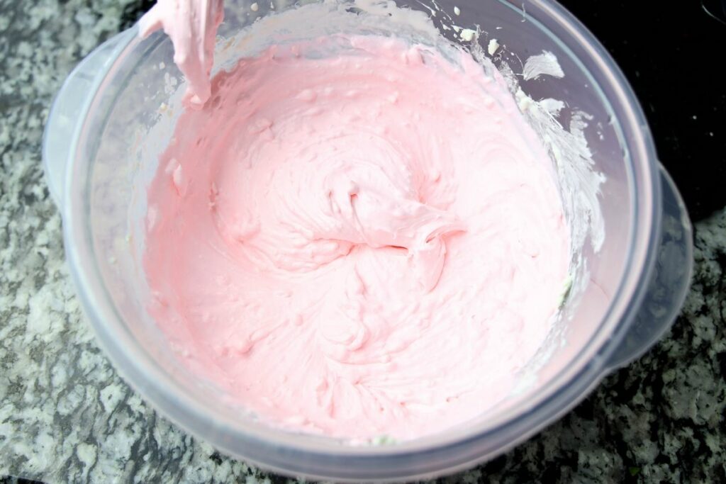 Cream cheese and whipped topping in a plastic bowl with pink food coloring.
